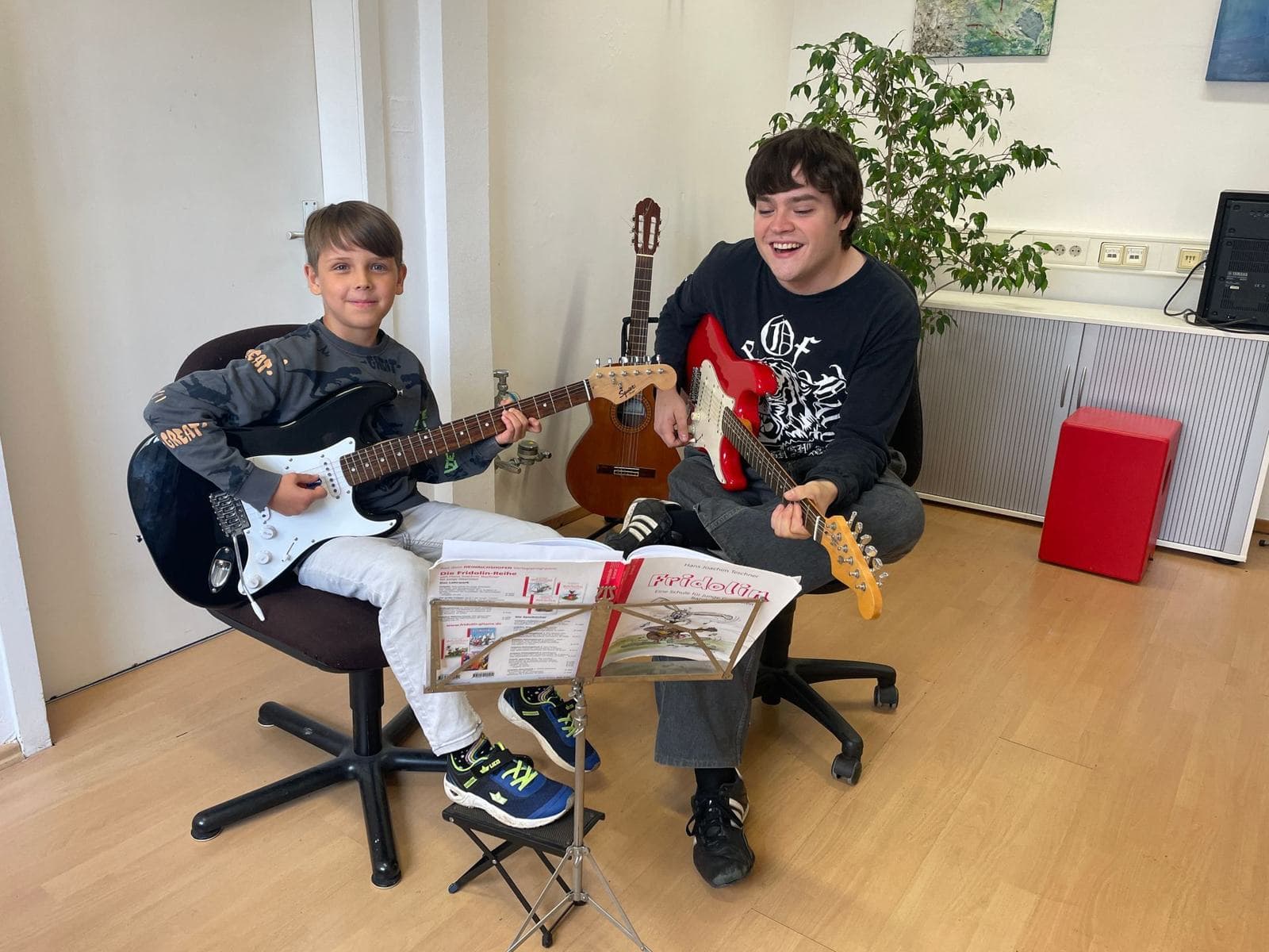Ein Junge und sein Lehrer spielen gemeinsam E-Gitarre und lachen.
