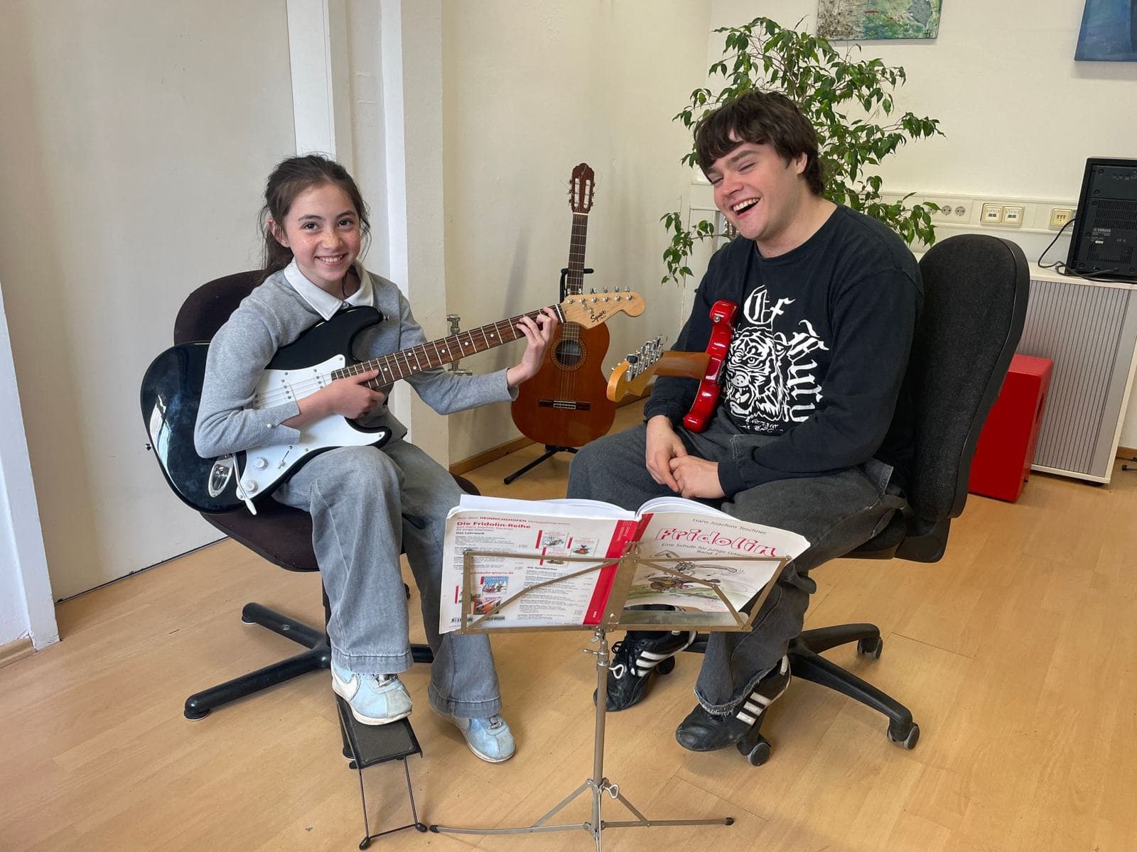 Eine Schülerin und ihr Gitarrenlehrer lachen während des Unterrichts.