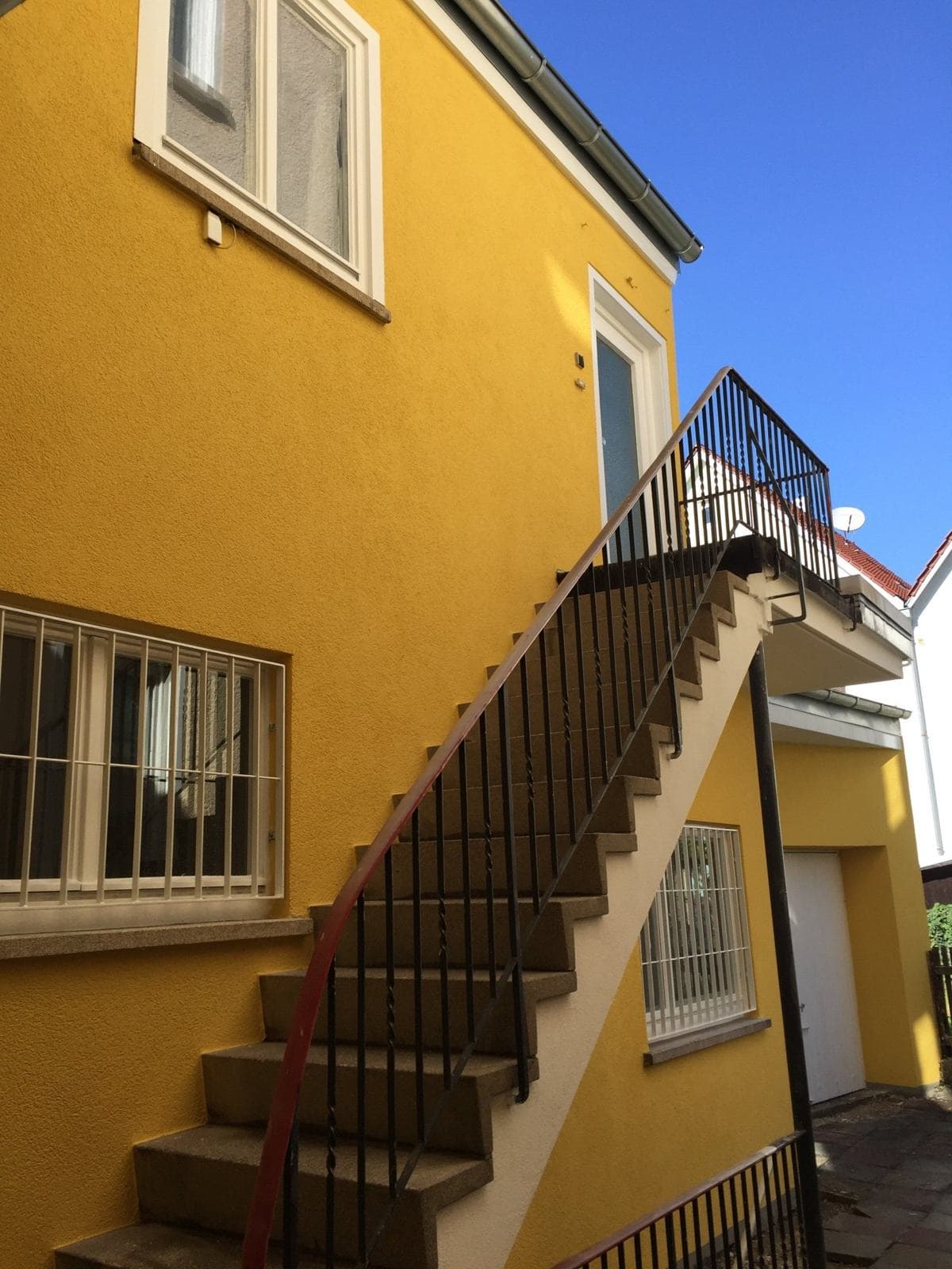Gelbe Fassade der Musikschule mit Außentreppe vor blauem Himmel.