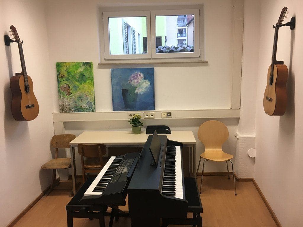 Unterrichtsraum mit Digitalpiano, zwei Gitarren an der Wand und Bildern.